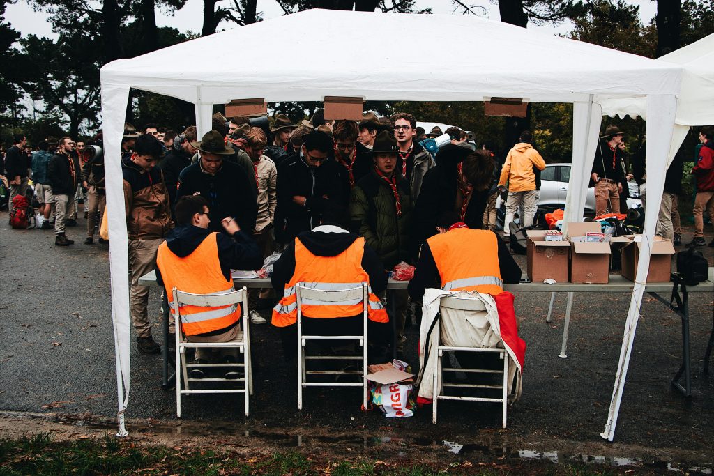 Crowded outdoor check-in tent at an event with attendees in fluorescent vests and scout uniforms.
